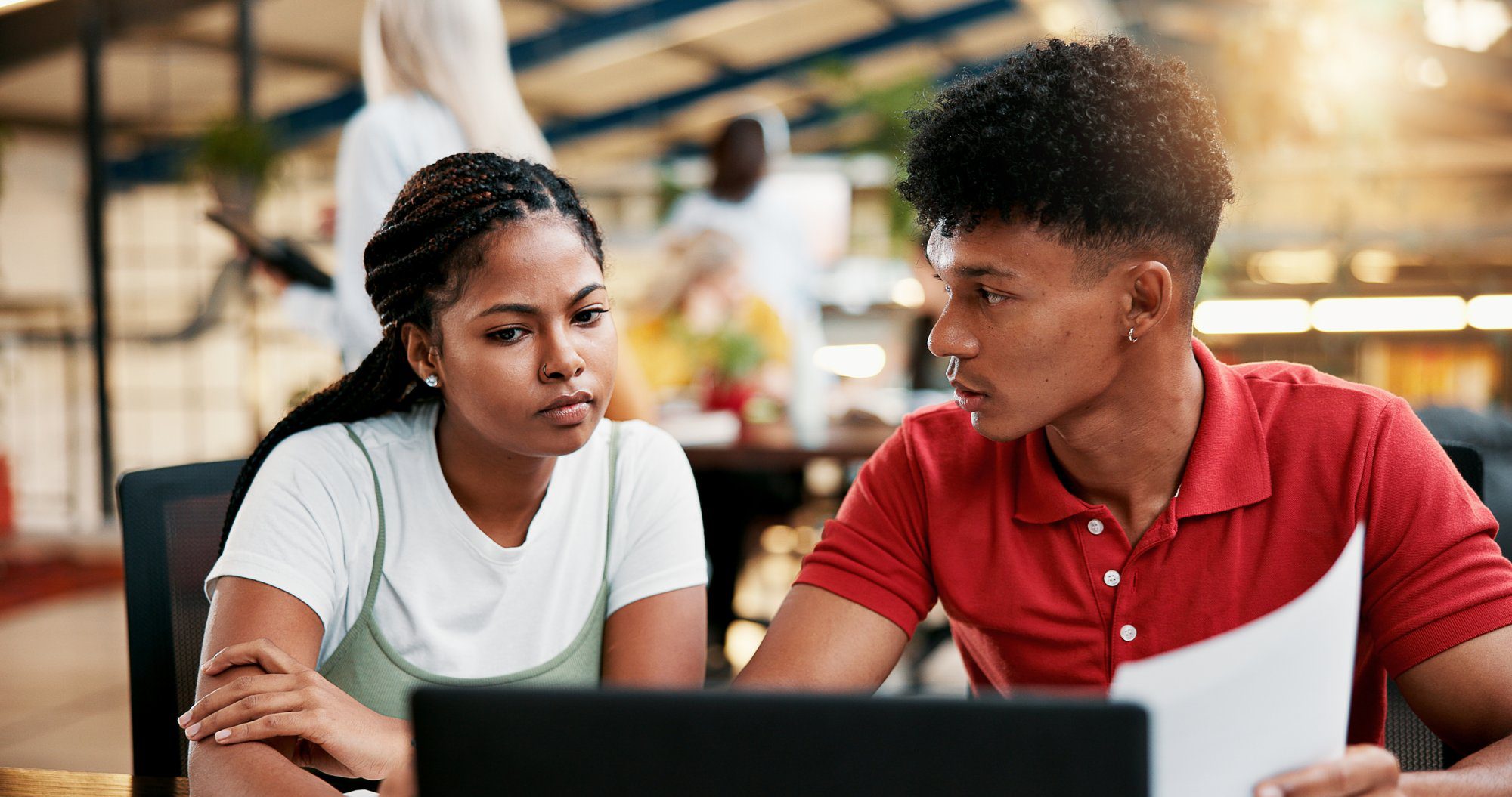 Two college students sitting together at a laptop, one holding a printed document